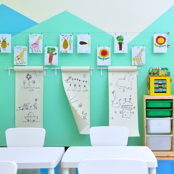 Children's drawings are hung on a turquoise and white wall. 
