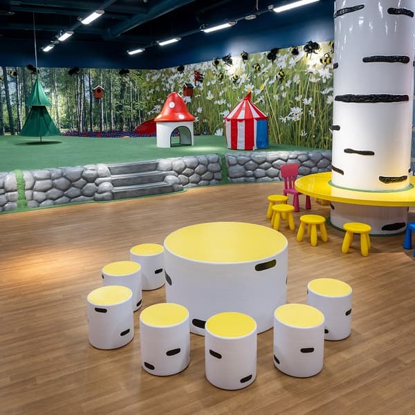 Children’s play area with tree-themed furniture, colourful stools, a circus tent and a magical forest backdrop.