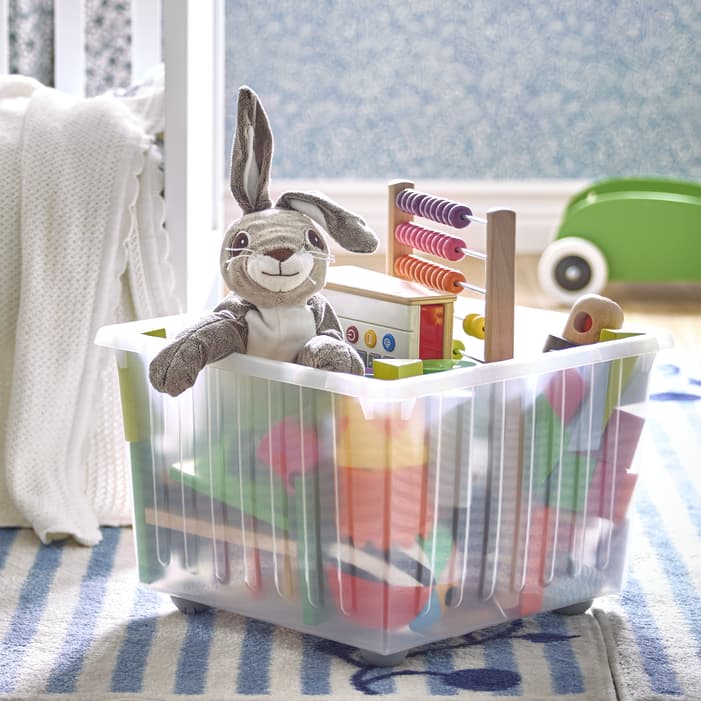 Children's plush toys, books and other playtime items in a children VESSLA storage box with wheels on top of a carpet in a child's room. 