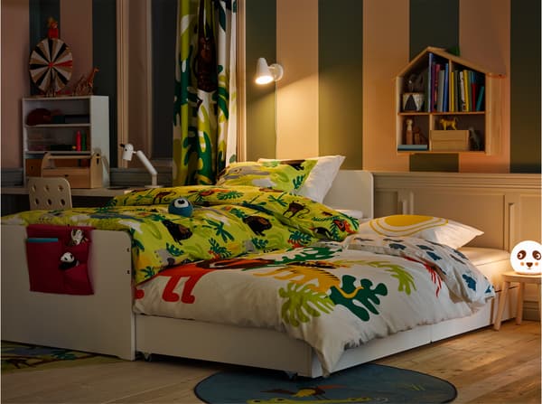 Children's room in an evening setting with a white bed frame with a rolled out underbed with bed textiles in animal prints.