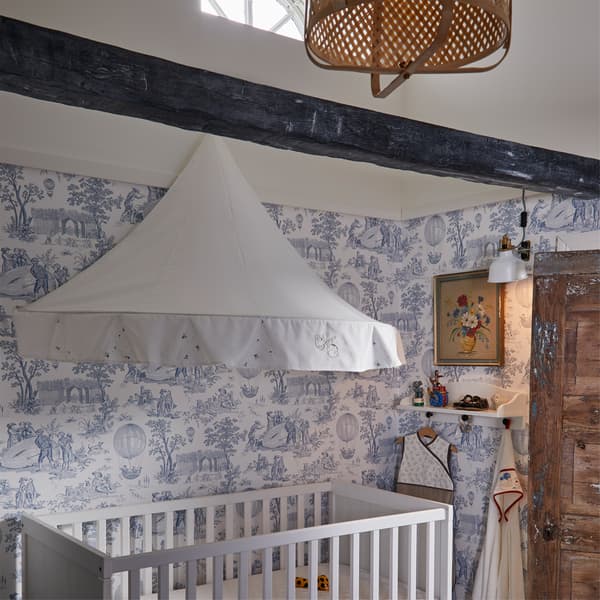 Children's room with a white bed canopy over a white cot, a pendant lamp in bamboo, and white wallpaper with a blue pattern.