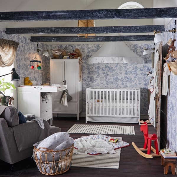 Children's room with blue/white wallpaper, a white cot and changing table, a white wardrobe and two white/black striped rugs.