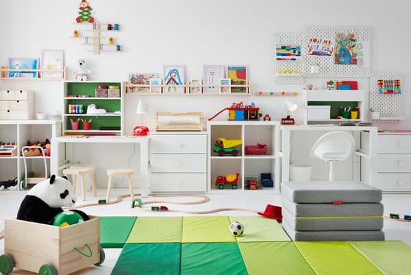 Children’s room with toys across the floor, desks along the side, and drawings on pegboards and FLISAT ledges up the walls.