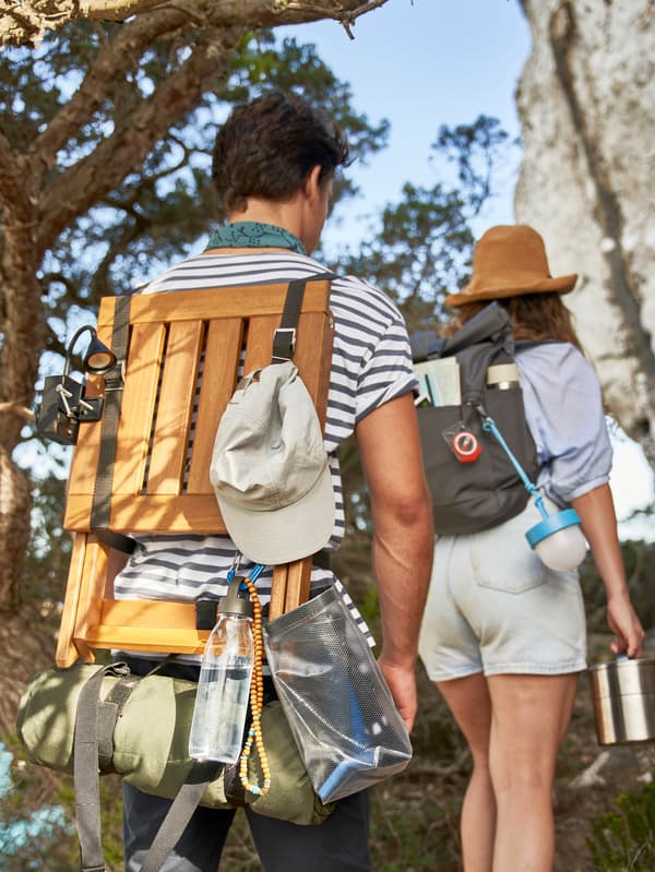 Chlapec a dievča stúpajú do kopca cez les, chlapec nesie na chrbte stoličku NÄMMARÖ, dievča nesie v ruke dvojposchodovú termosku FÖRSKAFFA.