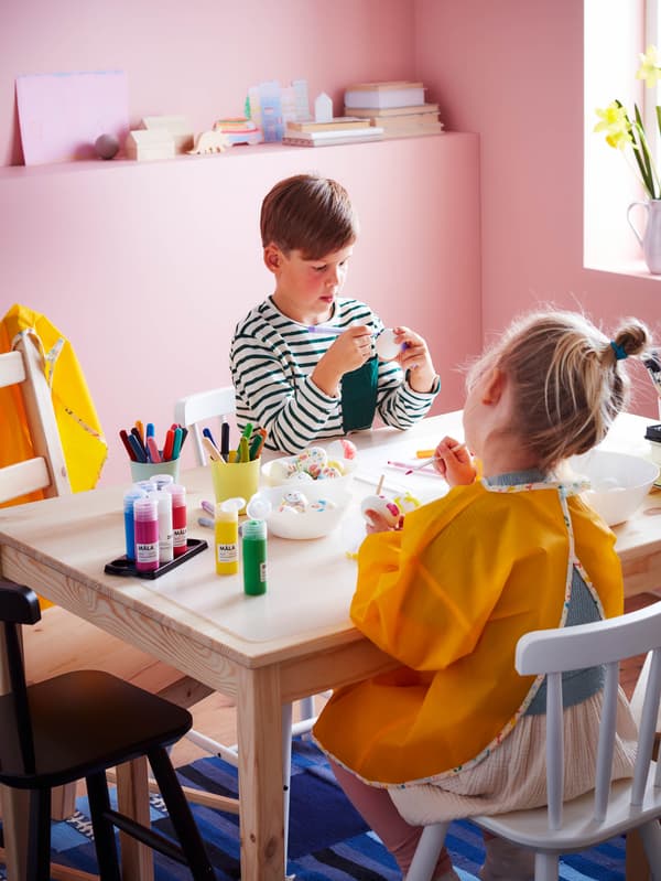 Chlapec a dievčatko ozdobujú vajíčka pri stole INGO.