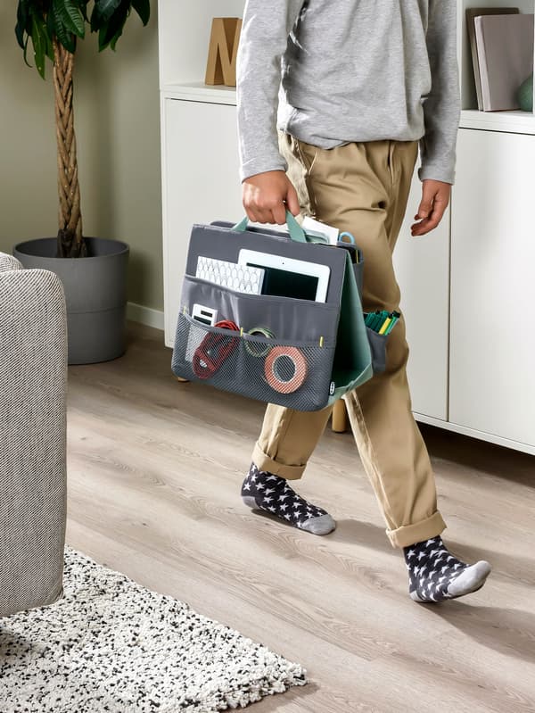 Chlapec kráča cez obývaciu izbu a nesie organizér kancelárskych potrieb ÖVNING.