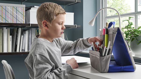 Chlapec s krátkými světlými vlasy u pracovního stolu, který si prohlíží školní potřeby.