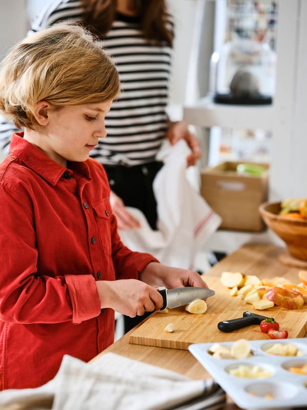 Chlapec v červenej košeli krája detským nožom SMÅBIT banán. 