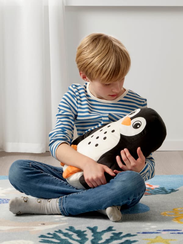 Chlapec v pruhovanom tričku drží v náručí vankúšik – tučniaka BLÅVINGAD.