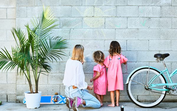 Chloé e le sue figlie disegnano con il gesso su una parete di mattoni grigi con accanto una pianta in vaso e una bicicletta celeste - IKEA