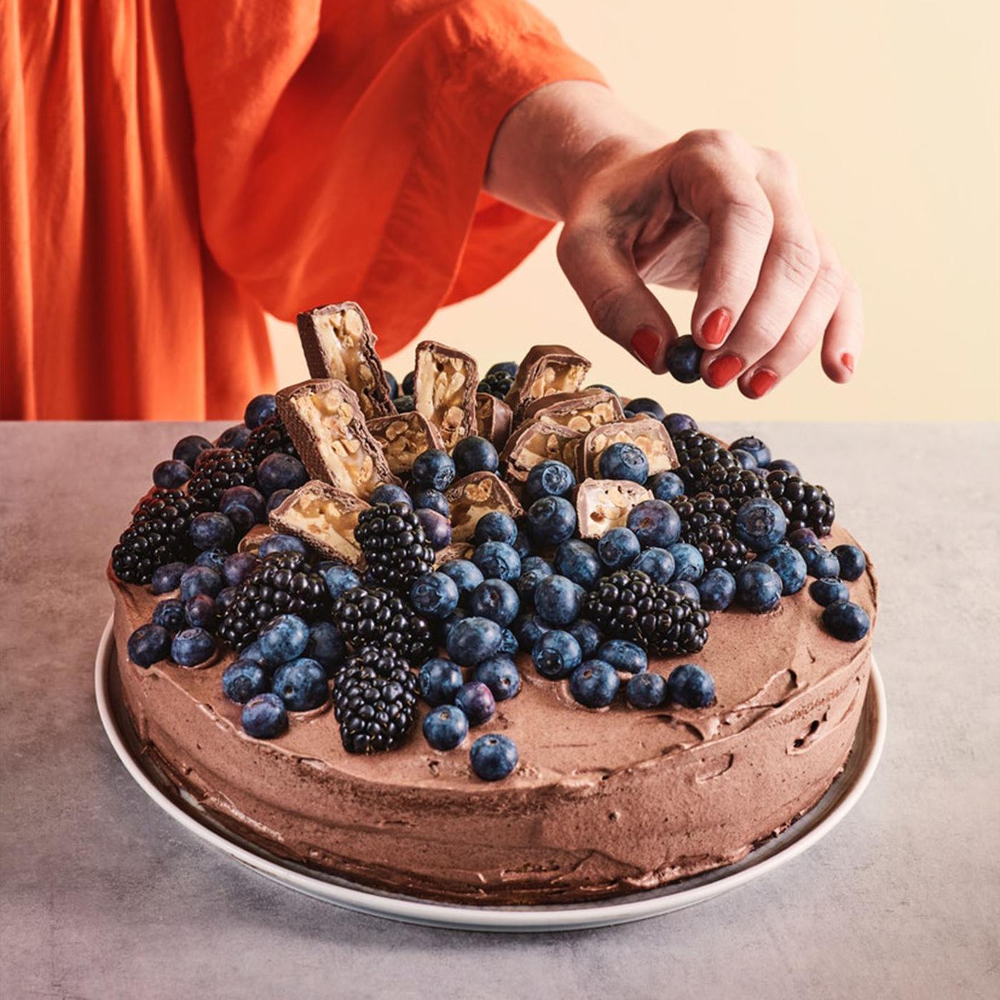 Chocoladetaart met bessen en stukjes chocolade; hand strooit blauwe bessen bovenop.