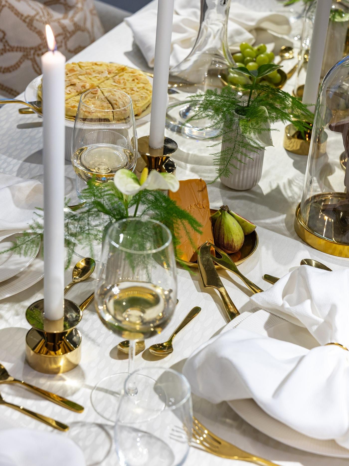 Chocolate bunny displayed under a glass dome at the centre of a softly styled table with candles, greenery and clear glassware.