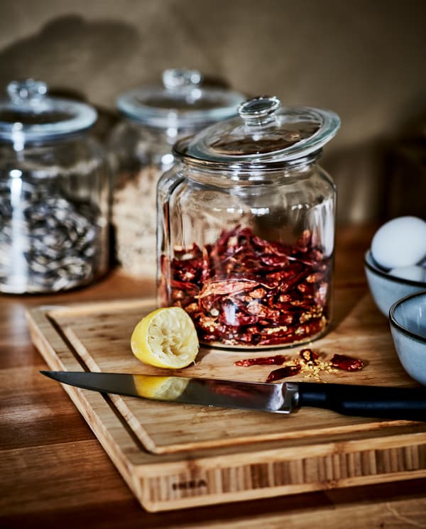 Chopped, dried chillies on a butcher’s block in bamboo, a knife, a squeezed lemon and a glass jar with more dried chillies.