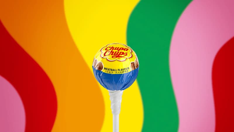 Chupa Chups Meatball Flavor lollipop inspired by IKEA dish on a colorful wavy background.