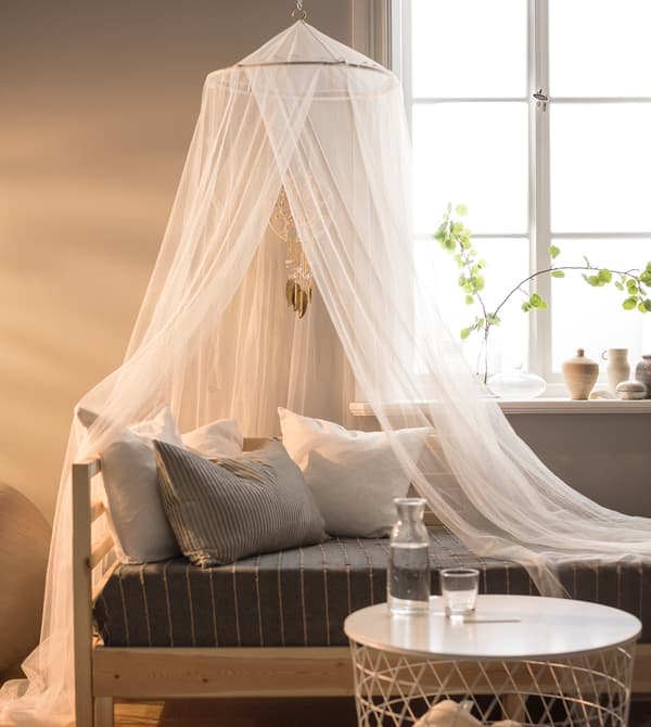 Ciel de lit et divan installés devant une fenêtre.