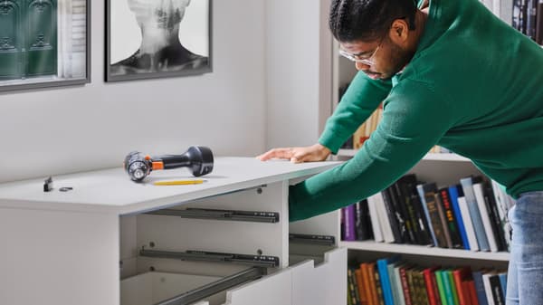 Cilvēks iebāž roku baltā NORDLI kumodē ar 7 atvilktnēm bez augšējām atvilktņu fasādēm, virspusē FIXA skrūvgriezi/urbi.
