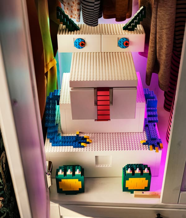 Cinq boîtes BYGGLEK blanches de différentes tailles sont placées pour former un monstre, avec des briques LEGO ajoutées pour définir ses traits.
