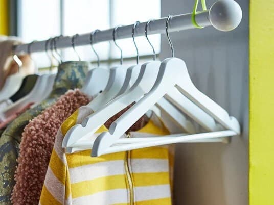 Cintres blancs dans une penderie, certains vides, certains portant des vêtements.