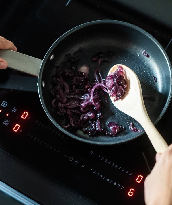 Cipolla che sta cuocendo in una padella su un piano a induzione. Un cucchiaio di legno la mescola.
