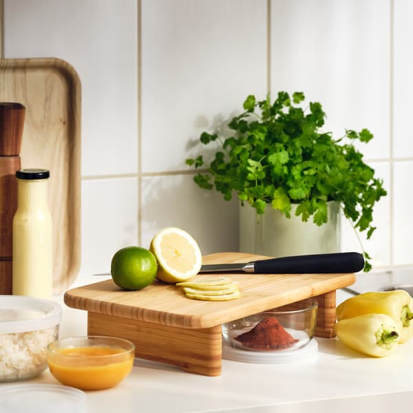 Citrusy a nůž na bambusovém prkénku STOLTHET na kuchyňské lince s čerstvými bylinkami a dalšími přísadami.