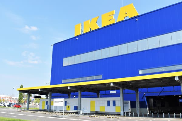 Clădirea magazinului IKEA, cu fațada albastră și galbenă, având logo-ul IKEA mare și galben în partea de sus. În fața clădirii se află o parcare cu locuri delimitate și un acoperiș pentru protecție. Cerul este senin.