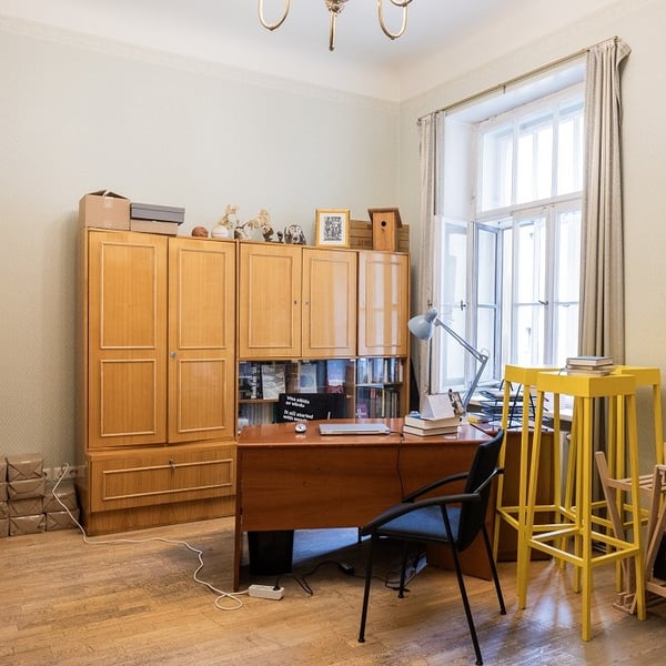 Classic home office with wooden desk, storage cabinets, large window, and yellow stools