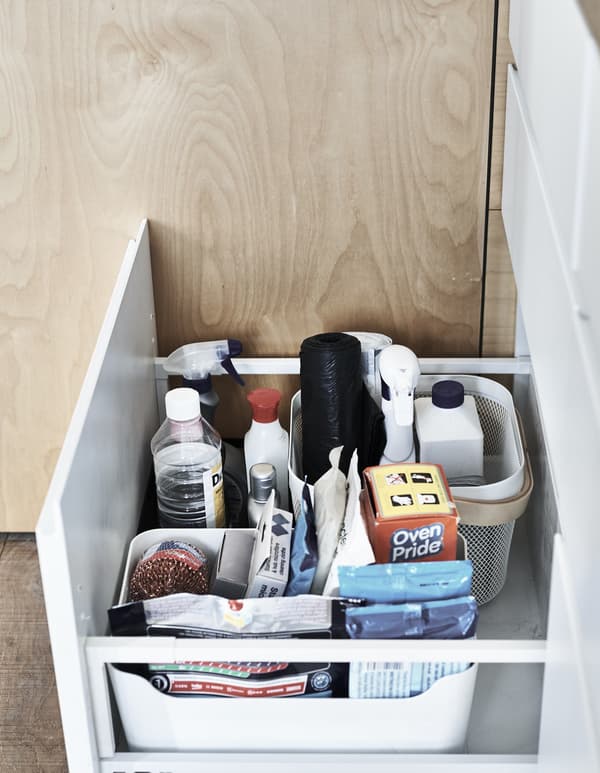 Cleaning products stored in boxes inside a open kitchen drawer.