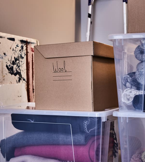 Clear plastic and paper boxes are stacked and store winter clothing in an attic.