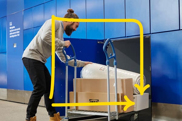 Client care își ridică singur comanda IKEA dintr-un dulap albastru de tip click & collect, încărcând pe cărucior cutii plate și o saltea rulat‑ambalată, evidențiate de un contur galben care arată traseul ușor al produselor.