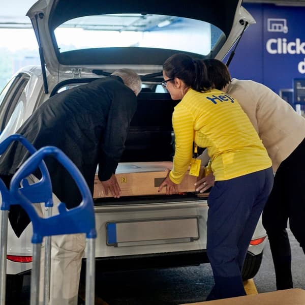 Client IKEA charge un grand meuble sur un chariot près d’un véhicule sur le parking.
