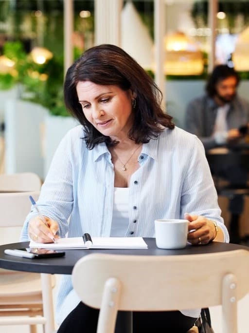 Clienta en un restaurant d’IKEA escrivint en una llibreta mentre pren un cafè.