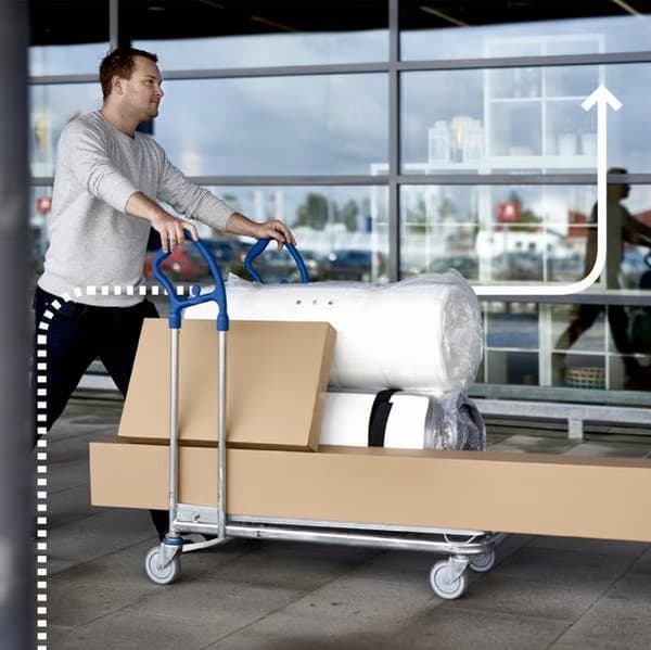 Cliente con un carro plano con muebles y un colchón de IKEA que acaba de comprar en la tienda