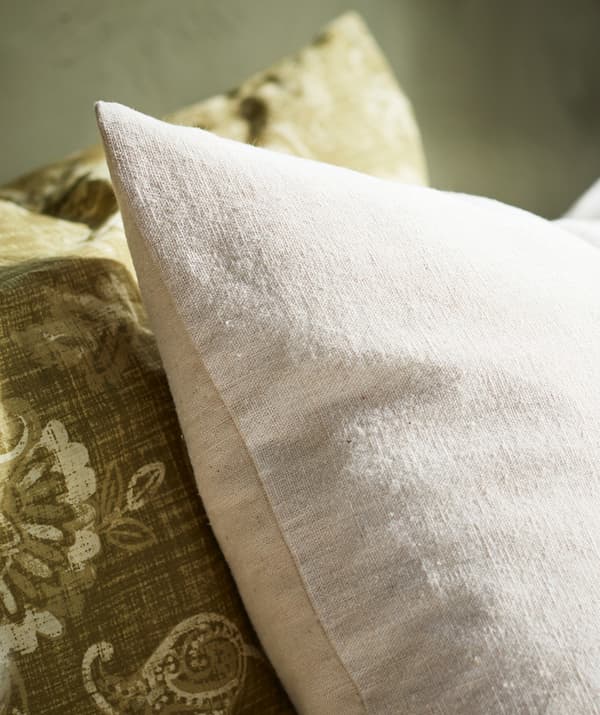 Close-up of a beige pillow in natural cotton material shown next to a green paisley patterned pillow.
