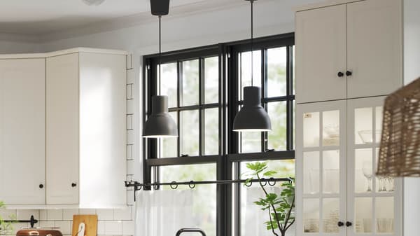 Close-up of a bright kitchen with black pendant lights, white cabinets, and large windows.
