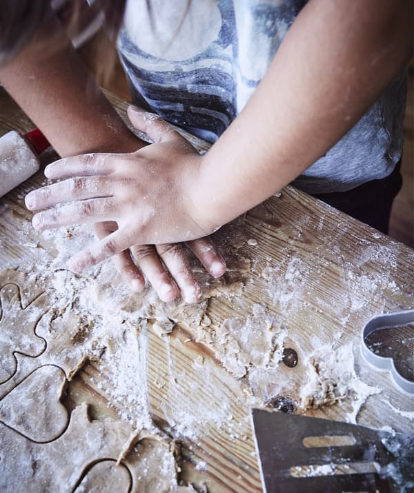 Close-up of a child cutting shapes in dough on a floured work surface.