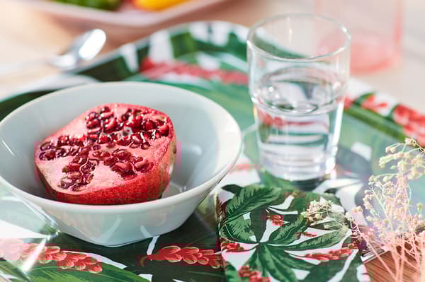 Close up of a crimson cut pomegranate, placed in a white bowl on a colourfully patterned tray.