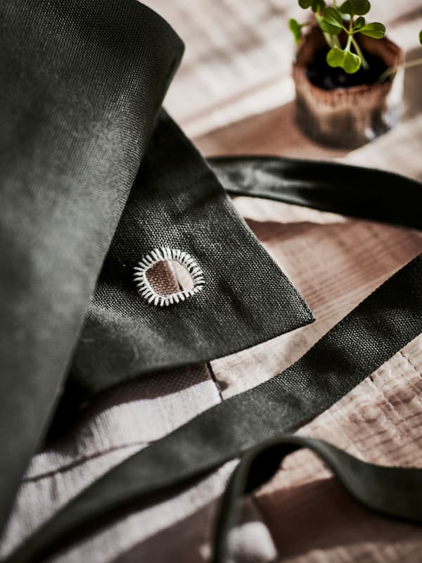 Close-up of a hand-embroidered detail on a dark green apron made in jute, shown on a table next to a small plant.