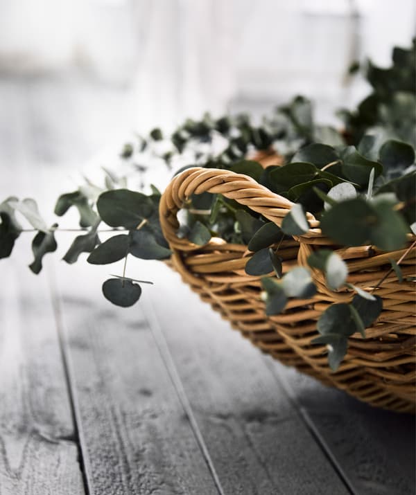 Close-up of a handle of a big, round TÄNKVÄRD rattan basket filled with blue-green eucalyptus leaves.