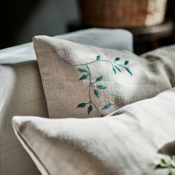 Close-up of a jute cushion cover decorated with hand-embroidered green leaves, shown in a beige sofa.