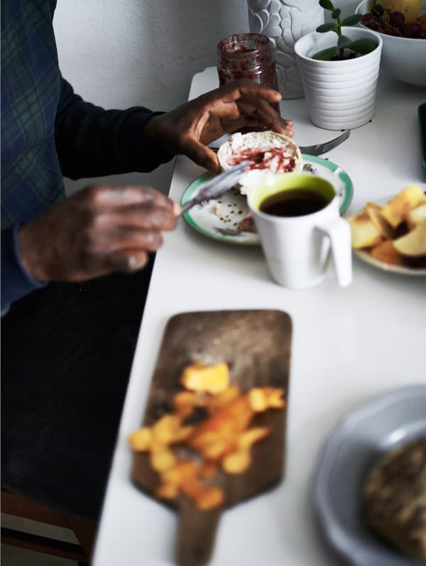 Close-up of a person spreading jam on bread at a table set with coffee and food.