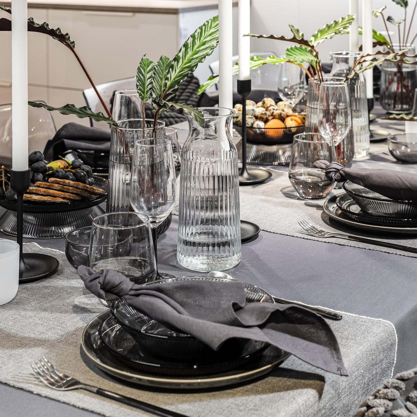 Close-up of a place setting with a dark plate, grey linen napkin, polished cutlery and clear glassware.