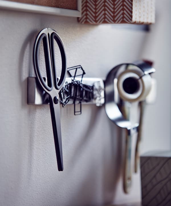 Close-up of a scissors, paperclips and tape hanging on a wall knife rack