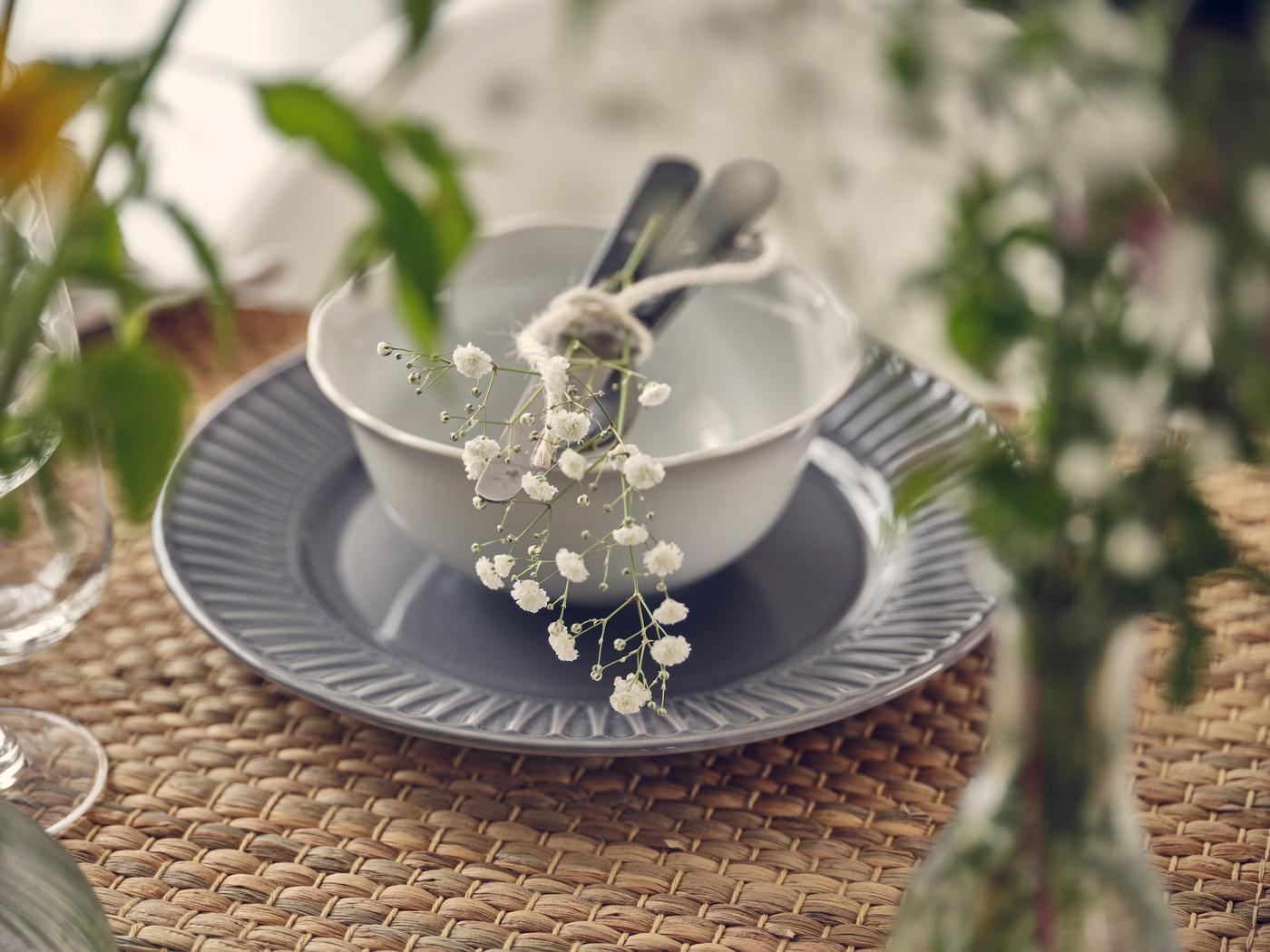 Close-up of a table setting with white bowl, grey plate, cutlery and delicate flowers.