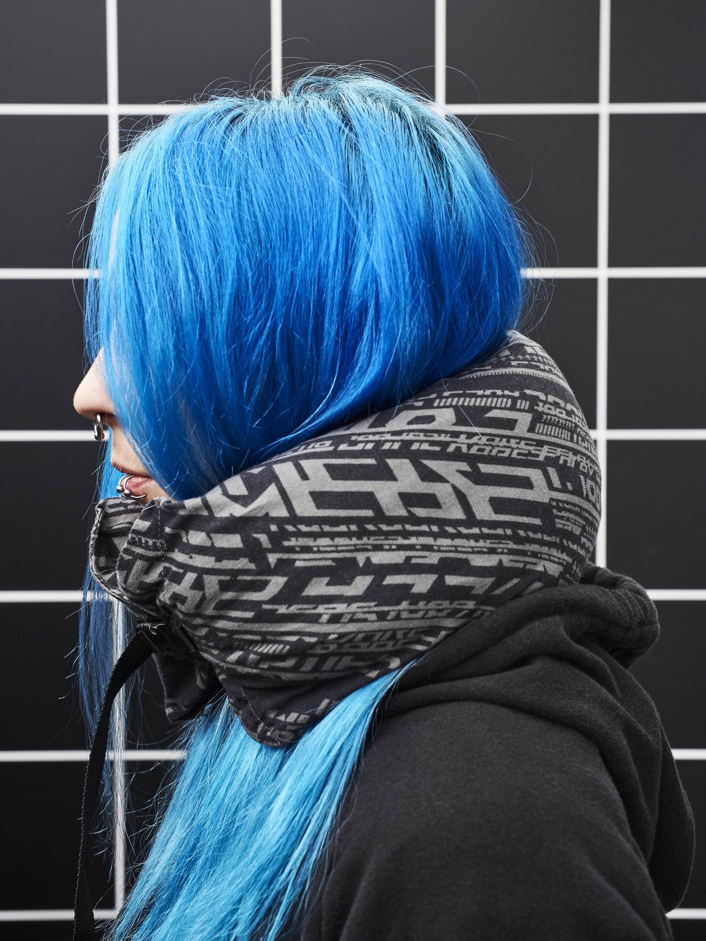 Close-up of a woman in profile. She has bright blue hair and a black hoodie and wears a LÅNESPELARE neck pillow.