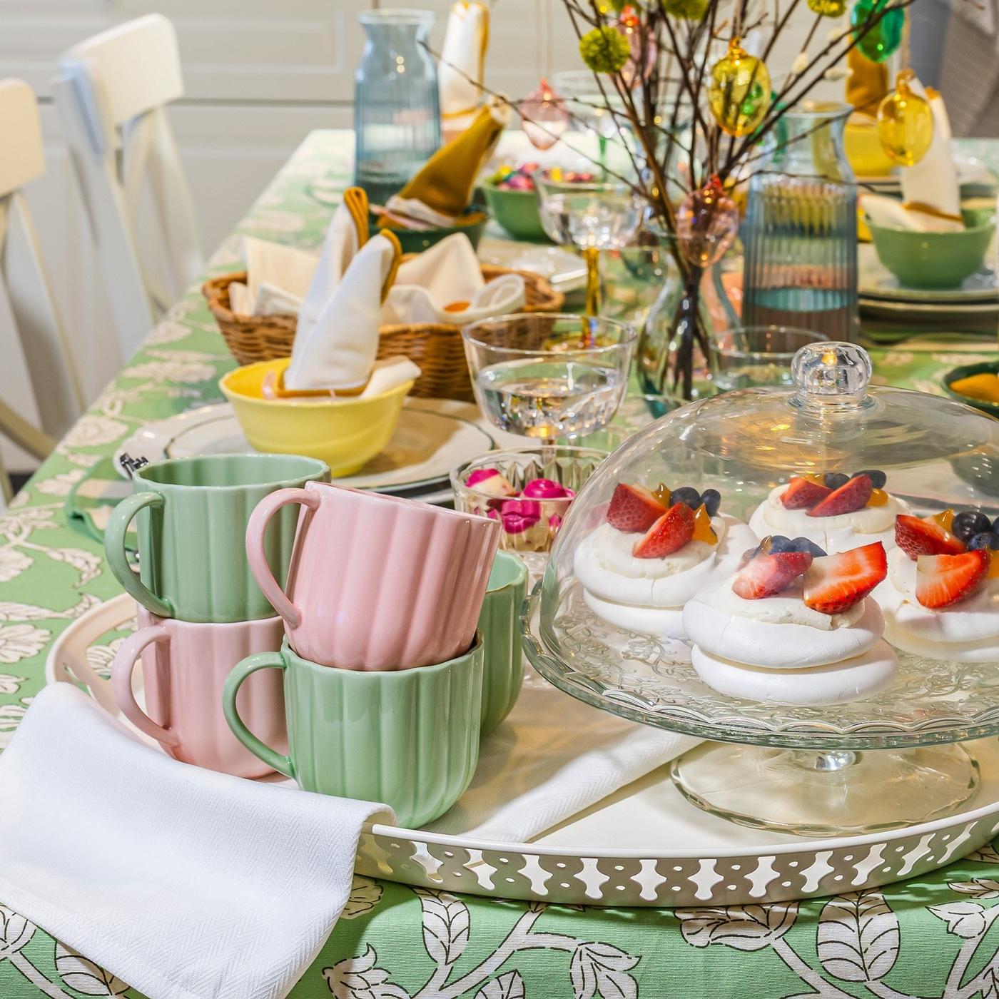 Close-up of an Easter table with pastel mugs, a cake stand and spring branches creating a playful, festive display.