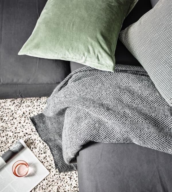Close-up of an IKEA STRIMLÖNN throw with herringbone design on a grey sofa, with a green cushion.