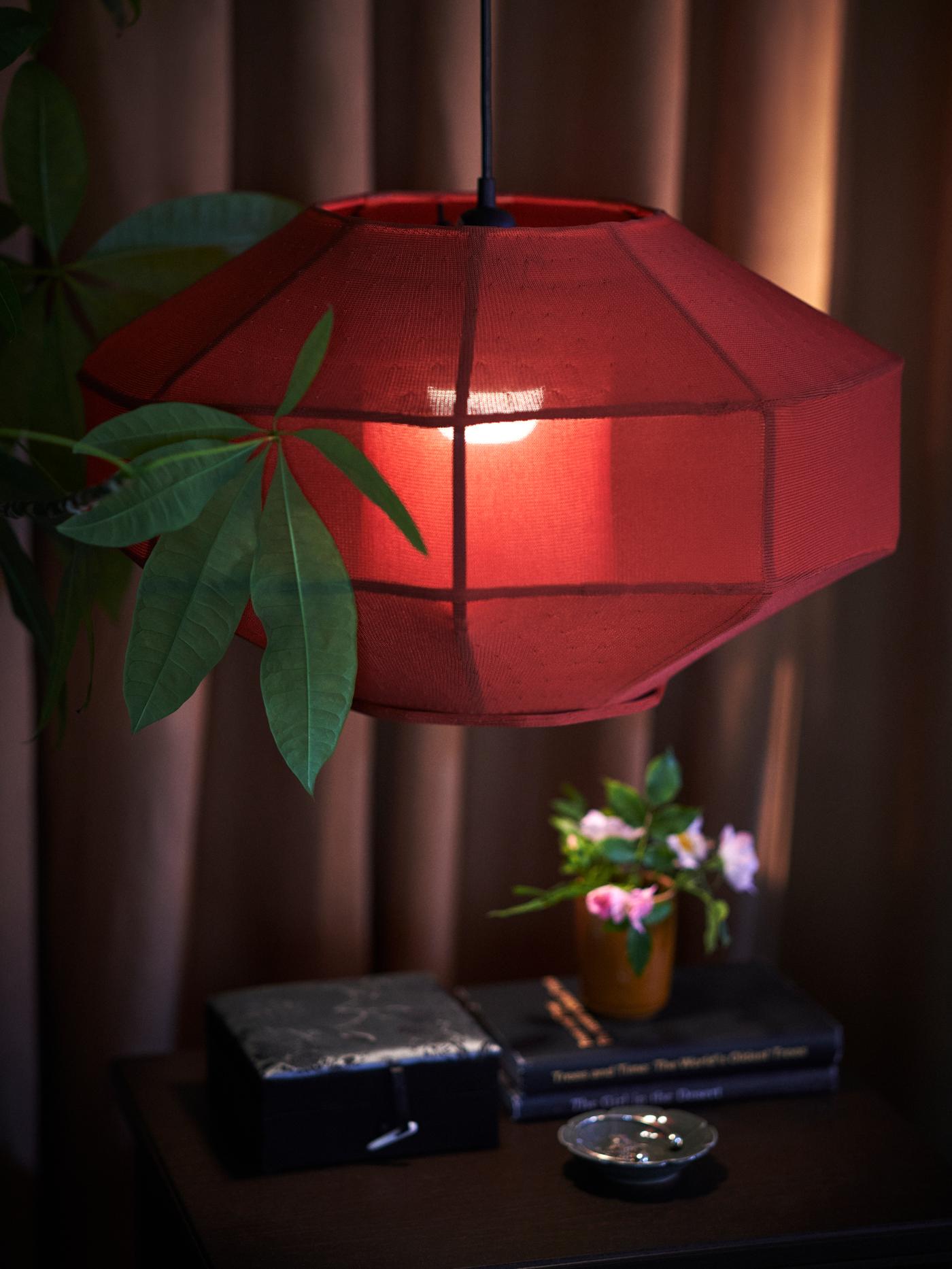 Close up of an illuminated lamp fitted with a FÖSSTA lampshade hanging in front of dark brown drapes.