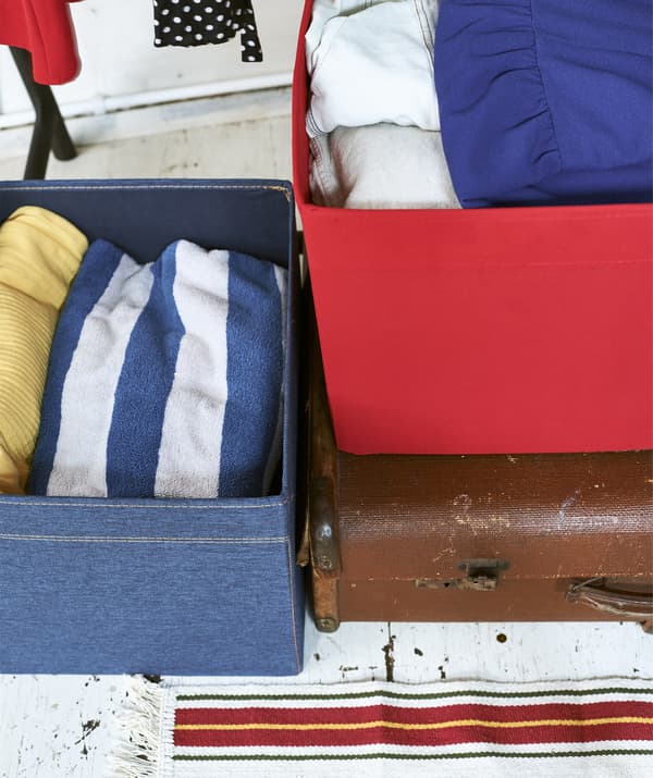 Close-up of denim and red storage boxes containing clothes on top of a suitcase.
