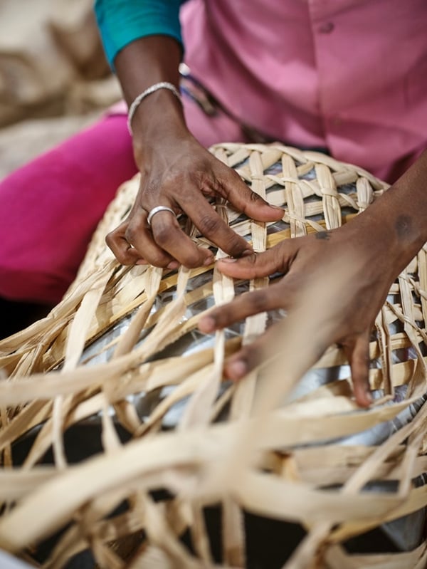 Close-up of hands weaving a MÄVINN basket from banana fibres and black cotton threads.