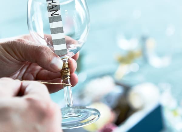Close-up of hands winding a thread around the stem of a wine glass.